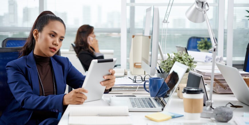 smartly-dressed-asian-woman-sitting-desk-office-with-tablet.jpg